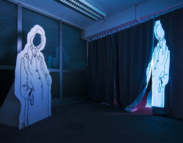 Figures of an "invisible woman" facing herself, mirrored in position. The woman on the left is a cut out character like you see at the seaside, and the woman on the right is a projected on a curtain. The room is dark and the woman are white with a black outline. They have no faces, hence they are "invisible".